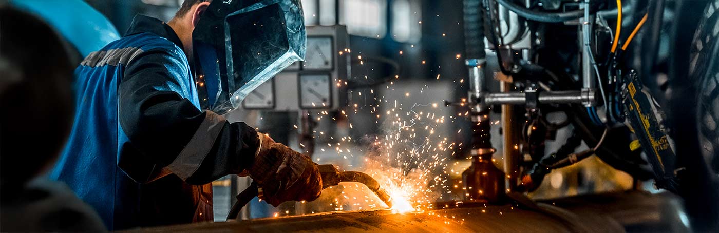 A welder wearing protective gear working on metal with sparks flying
